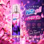 Dynamic product photography of Layer'r Wottagirl Amber Kiss Body Splash clear glass bottle with pink and purple fragrant mist cloud bursting beautifully from the pump nozzle, dozens of pink magenta and purple butterflies swirling dramatically in the mist, vibrant purple and pink background with glowing light bokeh, playful youthful feminine energy, fresh fragrant beauty campaign style, sharp product focus center, square 1:1 format, ultra cinematic magical whimsical shot